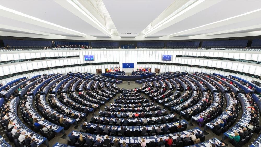 El hemiciclo del Parlamento Europeo. La obligación de la que trata el artículo no nace de la tecnología: nace de un reglamento aprobado aquí, y alcanza a empresas que no desarrollan nada.
     Se descartaron tres candidatas antes: un microcontrolador con la marca del fabricante bien visible —en un artículo del despacho parece un anuncio—, un mapa de centros de datos de Estados Unidos, que ni era fotografía ni venía a cuento en una web española, y una sala de servidores de un azul tan intenso que rompía la paleta de la casa.